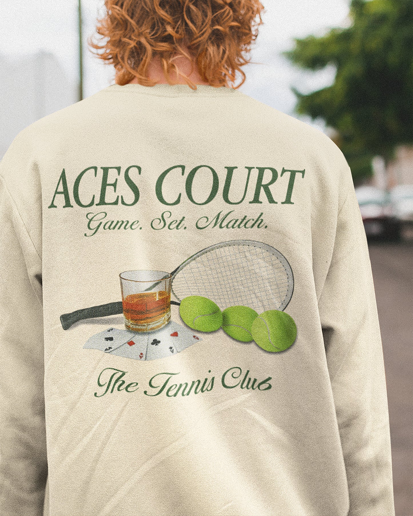 Person wearing a beige sweatshirt with 'ACES COURT' text and tennis-themed graphics.