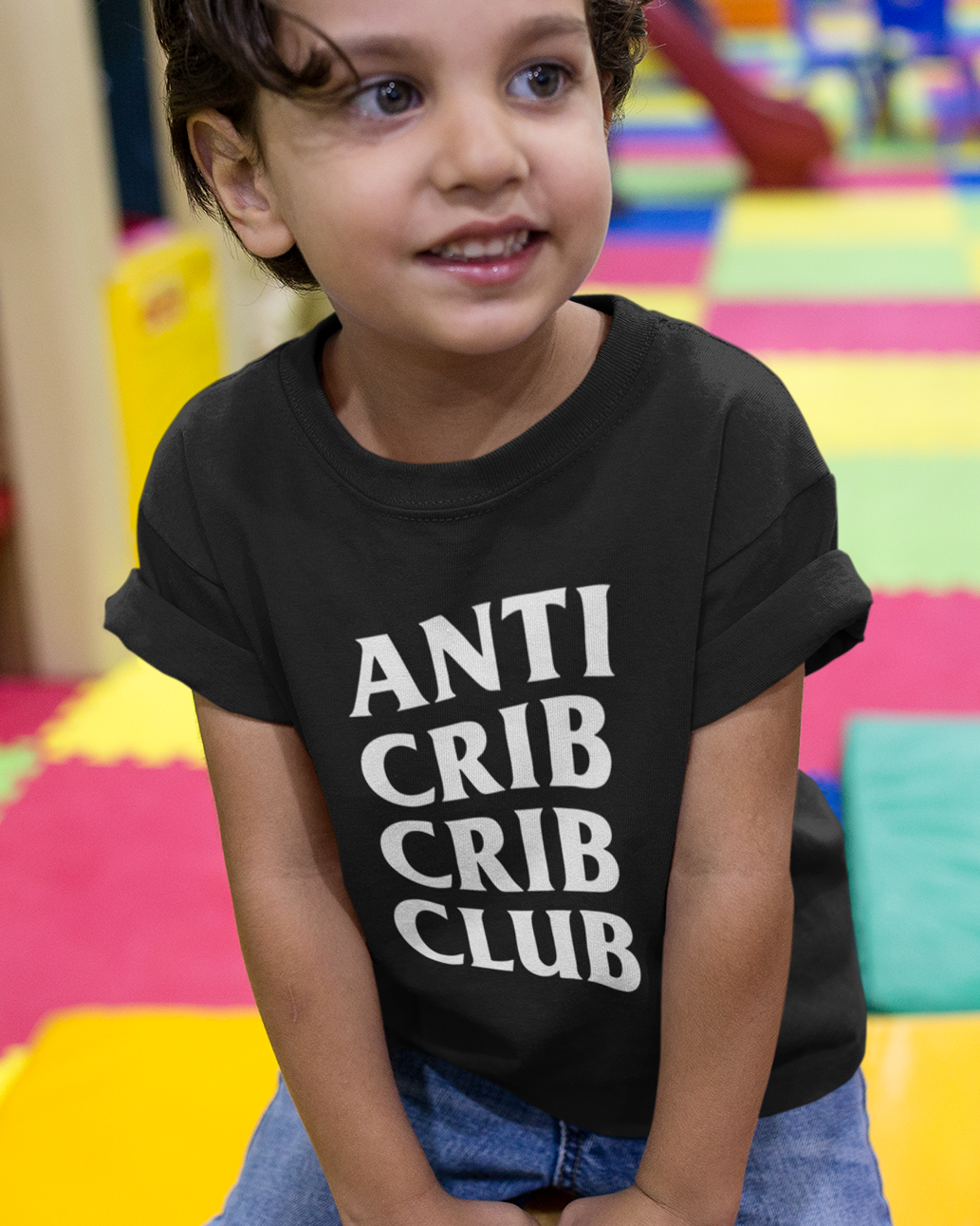 Child wearing a black t-shirt with 'ANTI CRIB CRIB CLUB' text in a colorful indoor setting