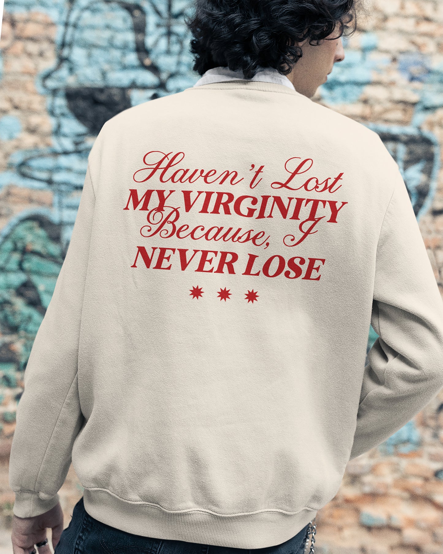 Person wearing a beige sweatshirt with I Never Lose graphic text against a graffiti-covered wall.