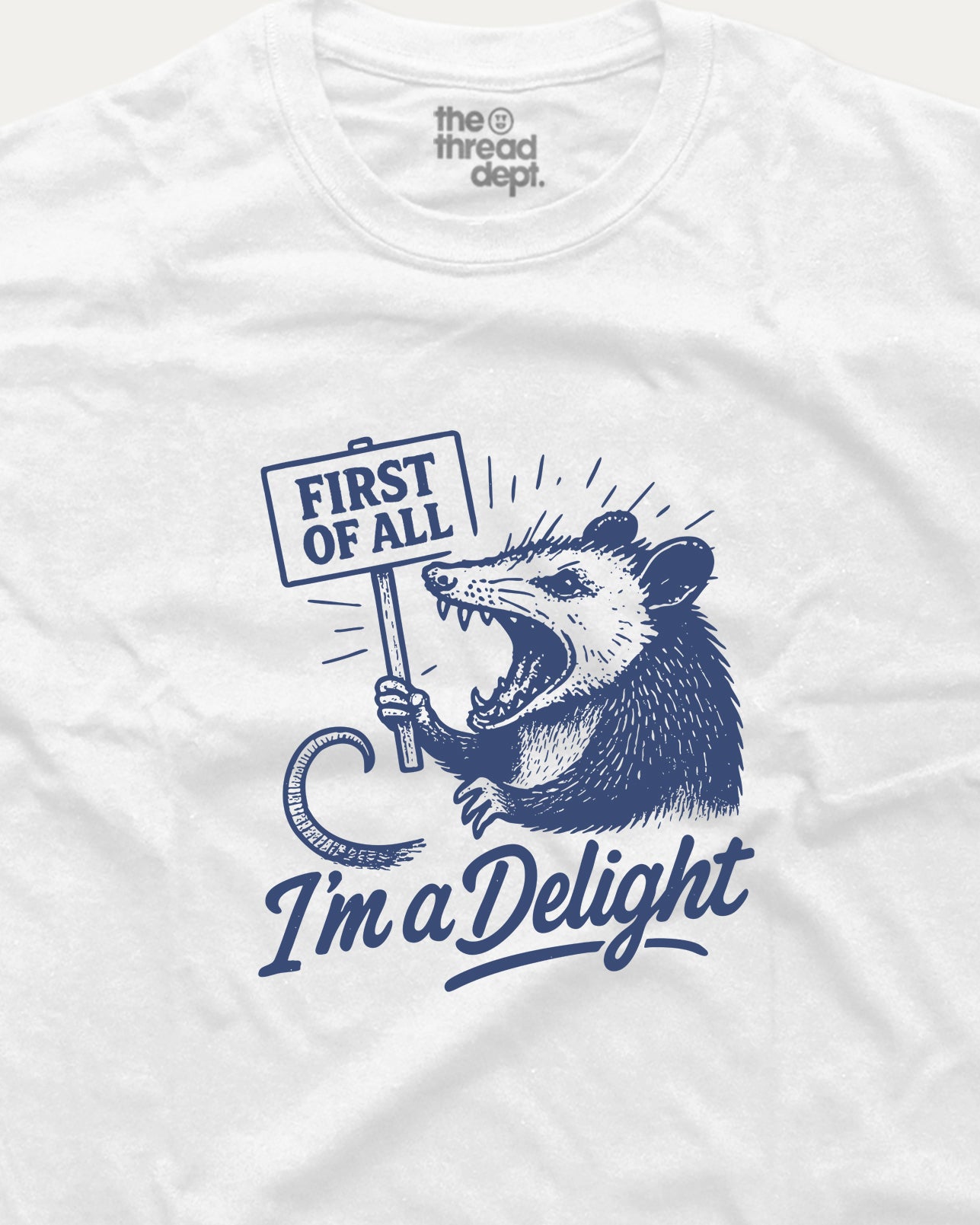 White t-shirt with a graphic of an opossum holding a sign and text 'First of All I'm a Delight' on a white background.
