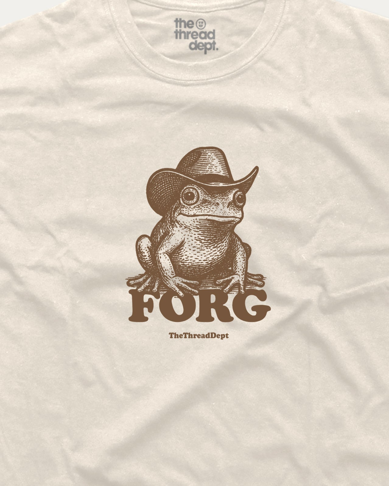 Beige t-shirt with a frog wearing a cowboy hat and 'FORG' text, brand 'the thread dept.' visible.