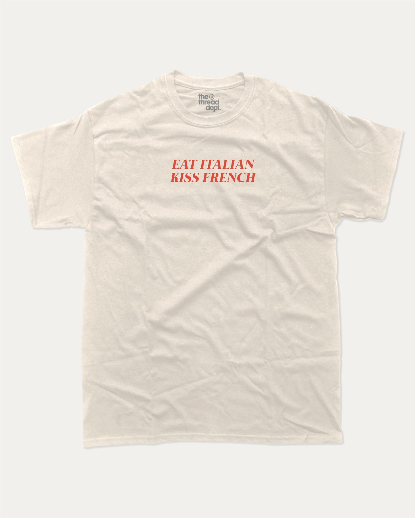 Eat Italian Kiss French graphic tee with bold and humorous print, funny and trendy graphic. Perfect for adults and gift-giving. Cream shirt.
