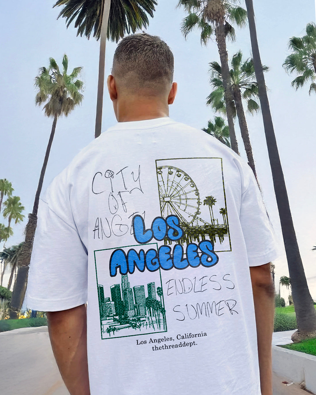 Person wearing a white t-shirt with 'Los Angeles' graphic in front of palm trees