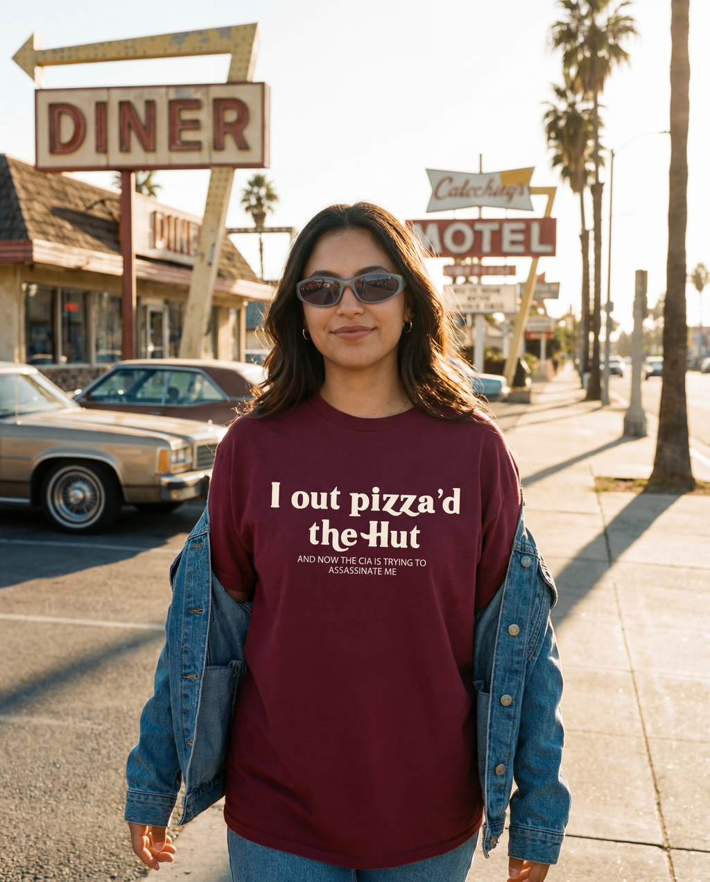 Woman wearing a maroon sweatshirt with text in front of a diner and motel sign.