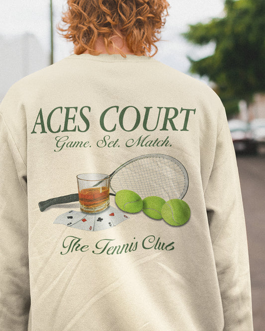 Person wearing a beige sweatshirt with 'ACES COURT' text and tennis-themed graphics.
