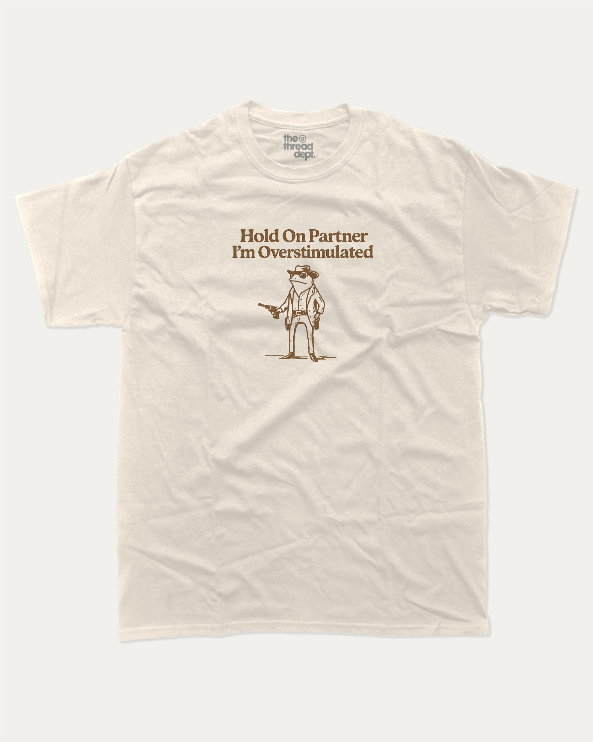 Hold On Partner I'm Overstimulated graphic t-shirt, perfect for adults. Funny Frogs tee, trending meme shirt, unique gift idea. Cream.