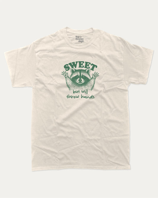 Sweet But Will Throw Hands Raccoon graphic t-shirt, perfect for gifts. Funny raccoon tee, trending meme shirt, unique gift idea. Cream.