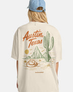 Person wearing a beige t-shirt with 'Austin, Texas' and desert graphics, standing against a white background.