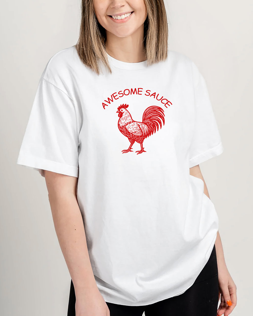 Person wearing a white t-shirt with a red rooster graphic and 'Awesome Sauce' text on a plain background