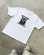 White t-shirt with a graphic of a raccoon and "become ungovernable" text on a concrete floor.