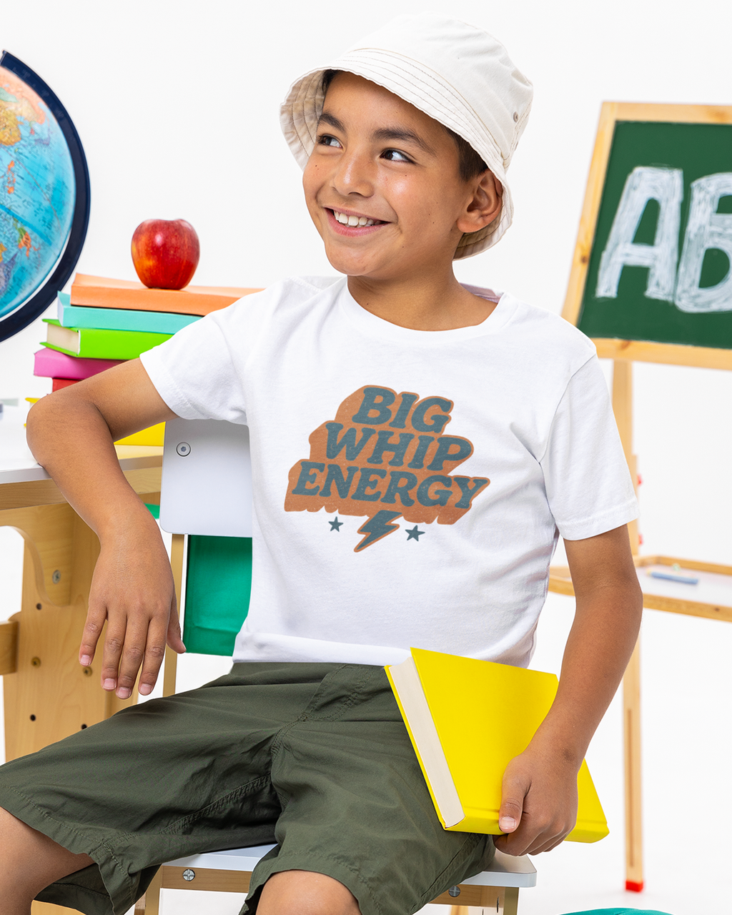Child wearing a white t-shirt with 'BIG WHIP ENERGY' text in a classroom setting