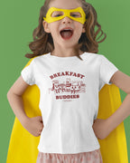 Child wearing a superhero costume with a 'Breakfast Buddies' t-shirt on a green background