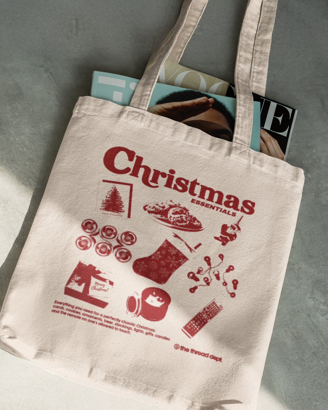 Beige tote bag with red Christmas illustrations and text on a gray surface