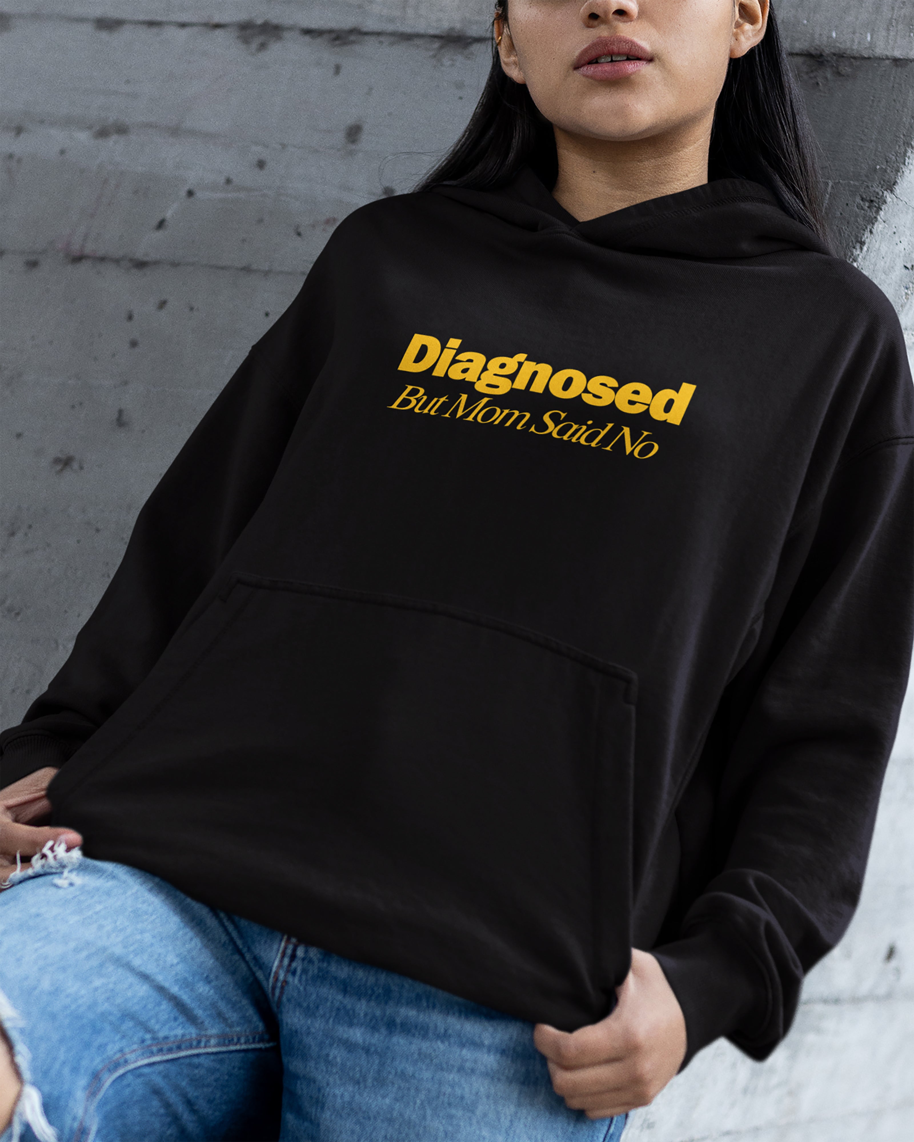 Person wearing a black hoodie with "diagnosed but mom said no" text against a gray wall.