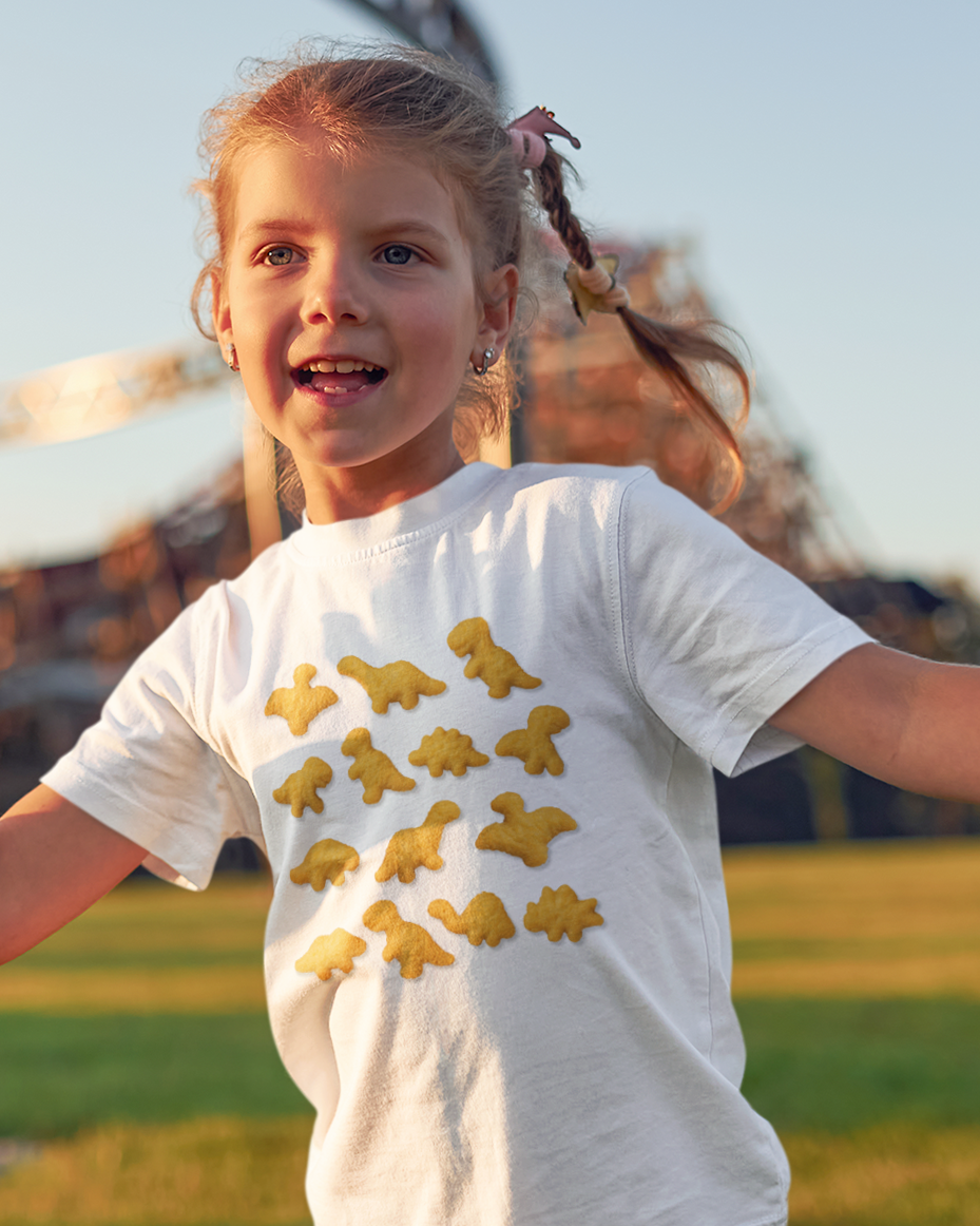 Young girl wearing a white t-shirt with yellow dinosaur prints outdoors.