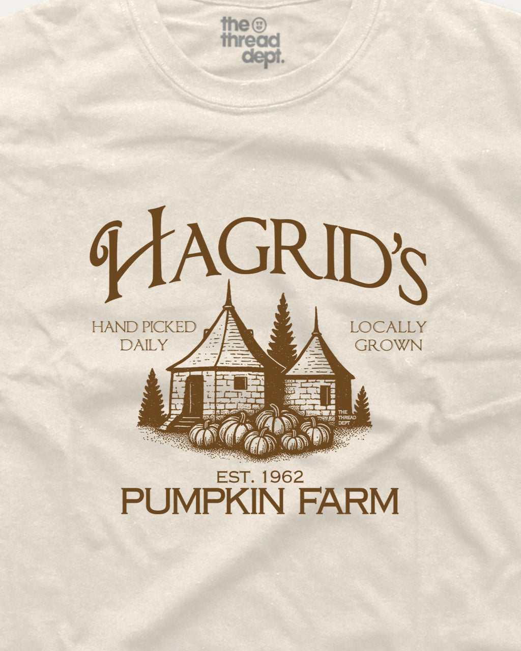 Beige t-shirt with brown graphic of a pumpkin patch and text 'Hagrid's Pumpkin Farm' on a beige background.