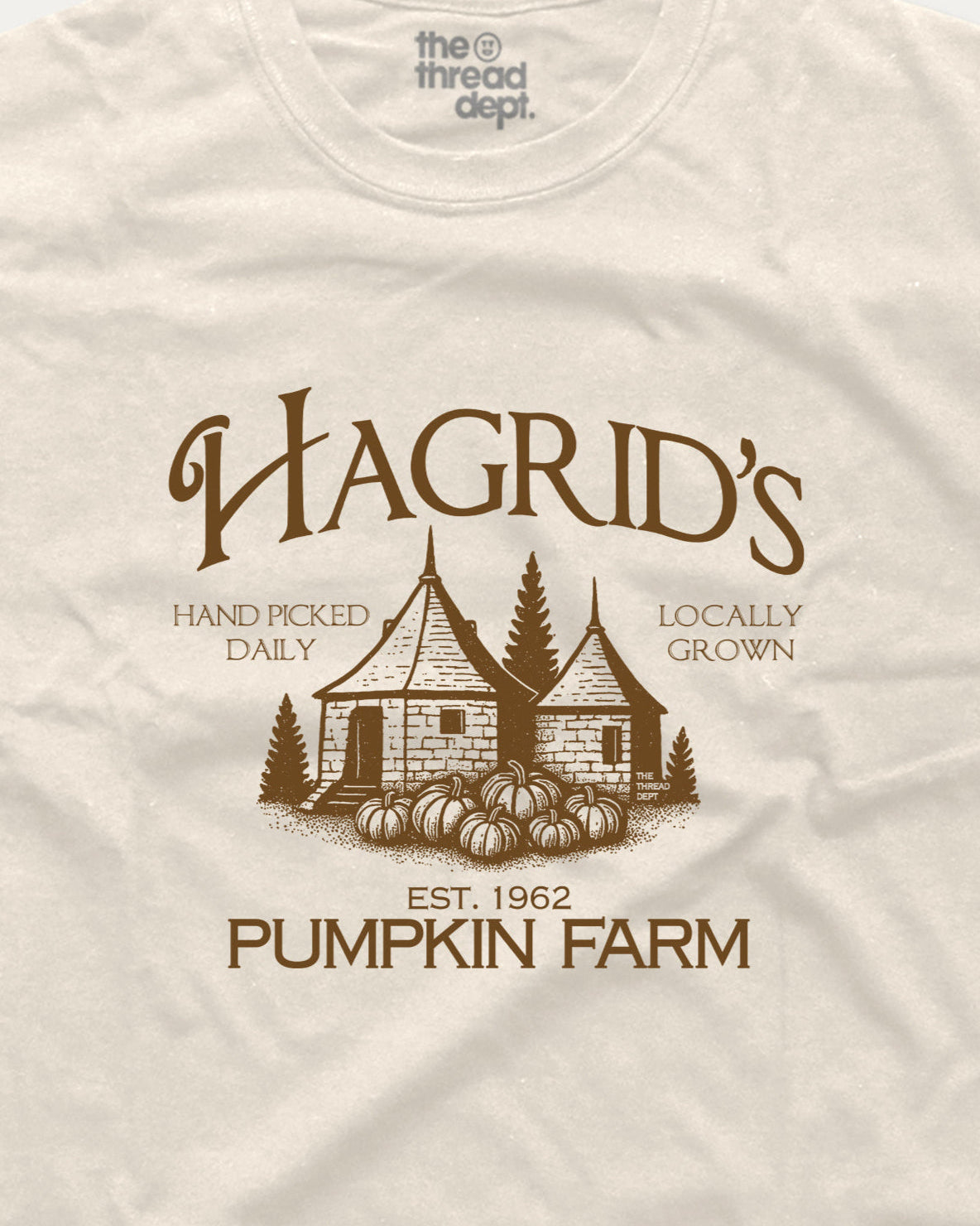 Beige t-shirt with brown graphic of a pumpkin patch and text 'Hagrid's Pumpkin Farm' on a beige background.