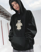 Person wearing a black hoodie with a graphic design of a cat-like creature on a white background.