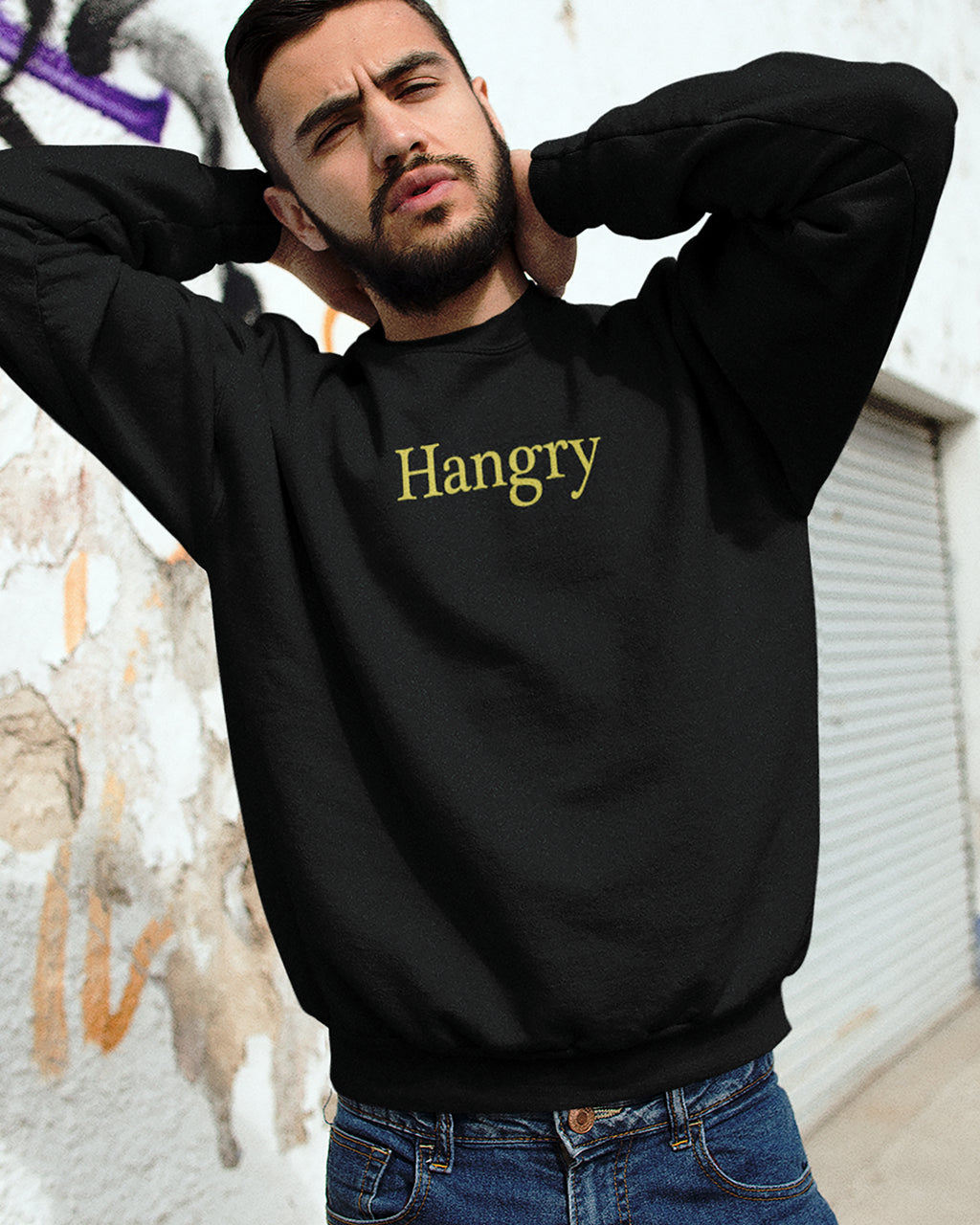 Man wearing a black sweatshirt with 'Hangry' text, standing against a wall.