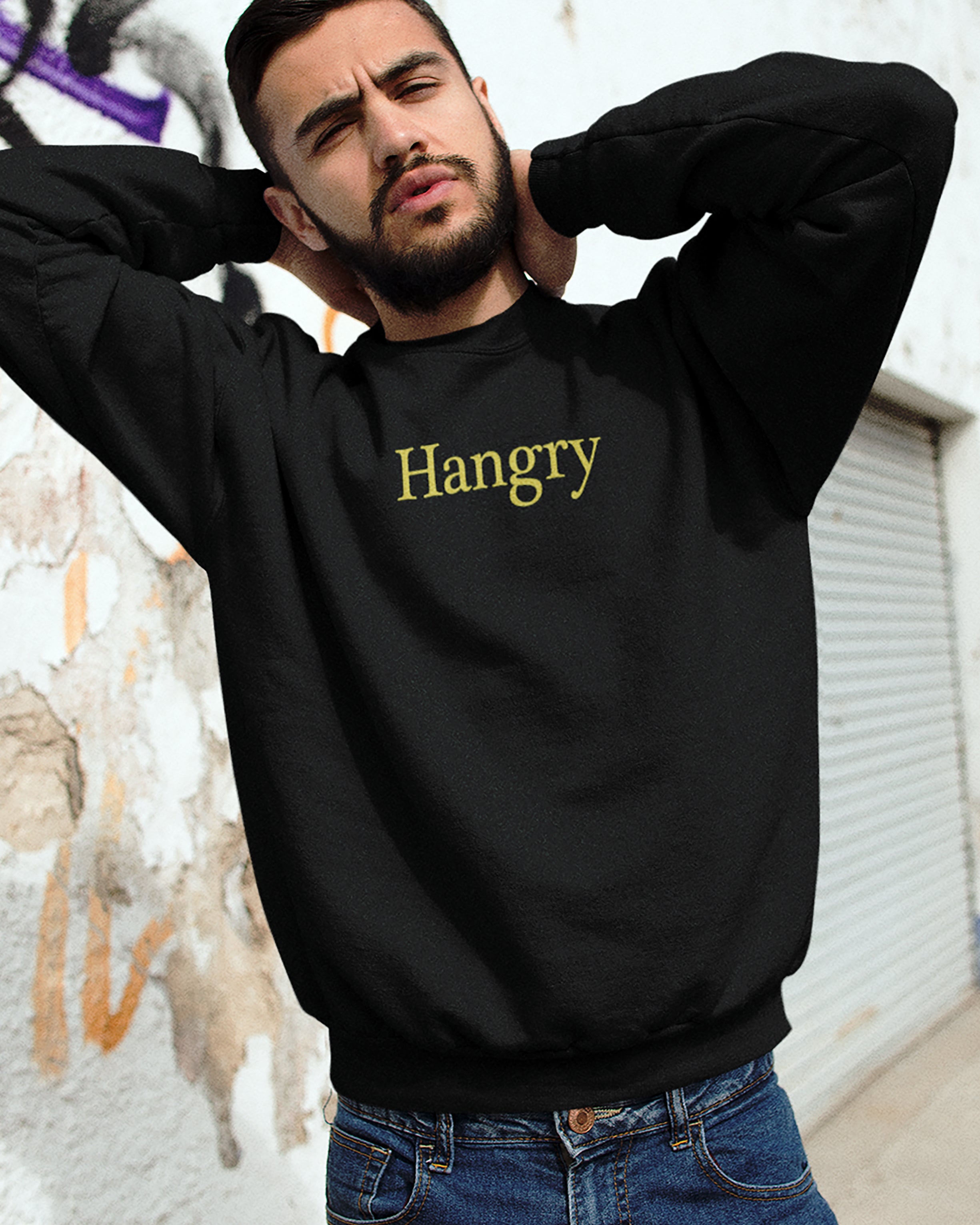 Man wearing a black sweatshirt with 'Hangry' text, standing against a wall.