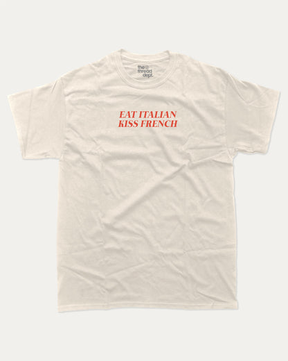 Eat Italian Kiss French graphic tee with bold and humorous print, funny and trendy graphic. Perfect for adults and gift-giving. Cream shirt.