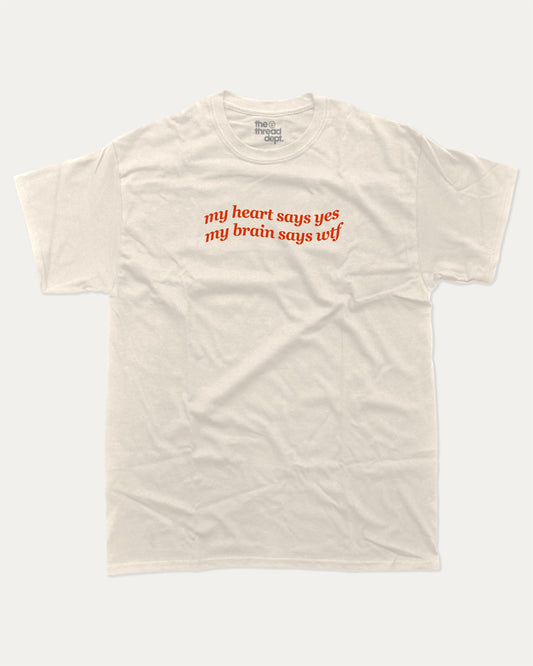my heart says yes my brain says wtf graphic tee with bold and humorous print, funny and trendy graphic. Perfect for adults and gift-giving. Cream shirt.