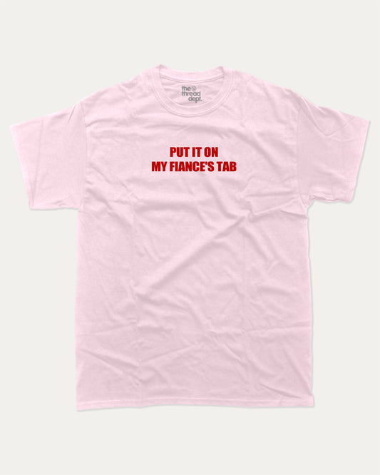 Put It On My Fiance's Tab graphic tee with bold and humorous print, funny and trendy graphic. Perfect for adults and gift-giving. Pink shirt.