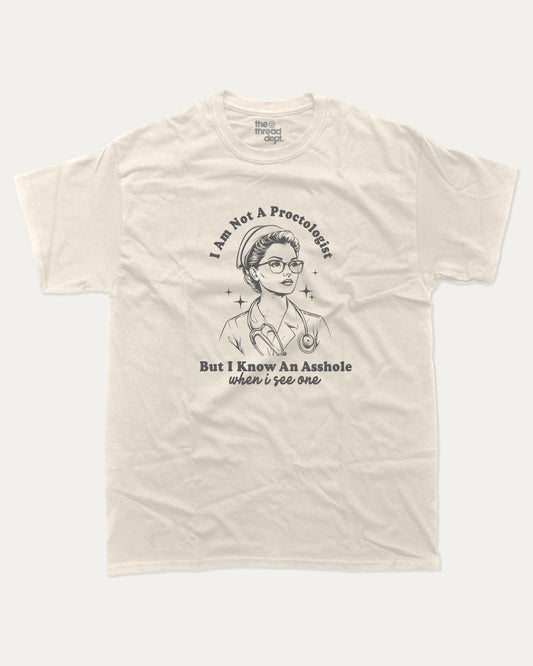 Beige t-shirt with I am not a Proctologist but I know asshole when I see one graphic and text on a white background