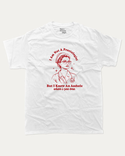 White t-shirt with I am not a Proctologist but I know asshole when I see one graphic and text on a white background