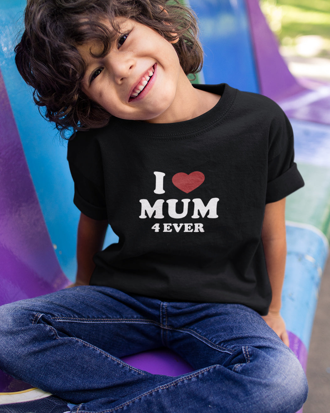 Child wearing a black t-shirt with 'I Love MUM 4 EVER' text, sitting on a colorful slide.