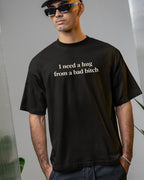 Person wearing a black t-shirt with text, standing against a neutral background