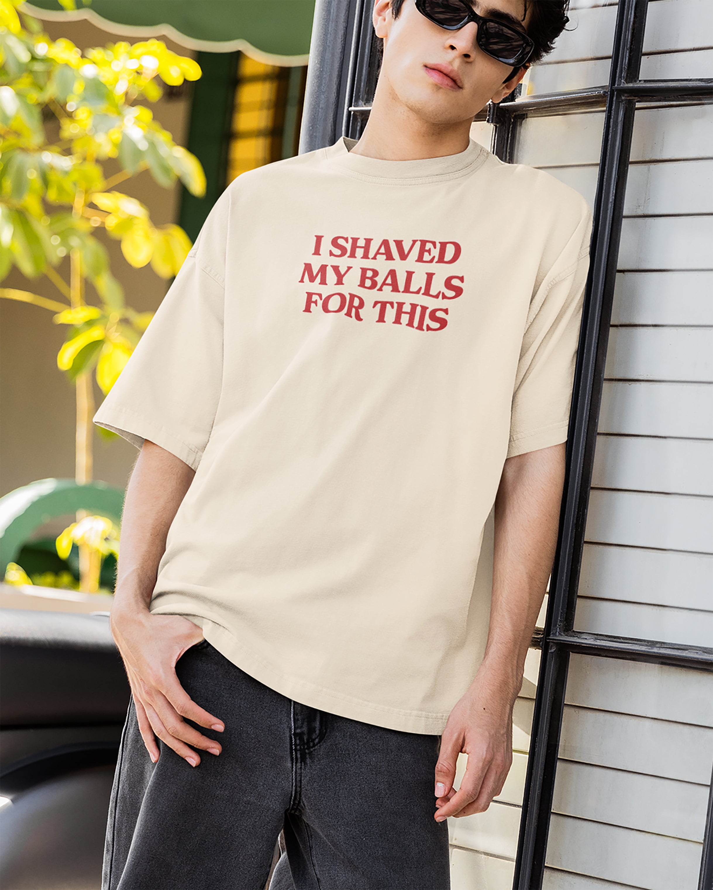 Person wearing a beige t-shirt with red text outdoors.