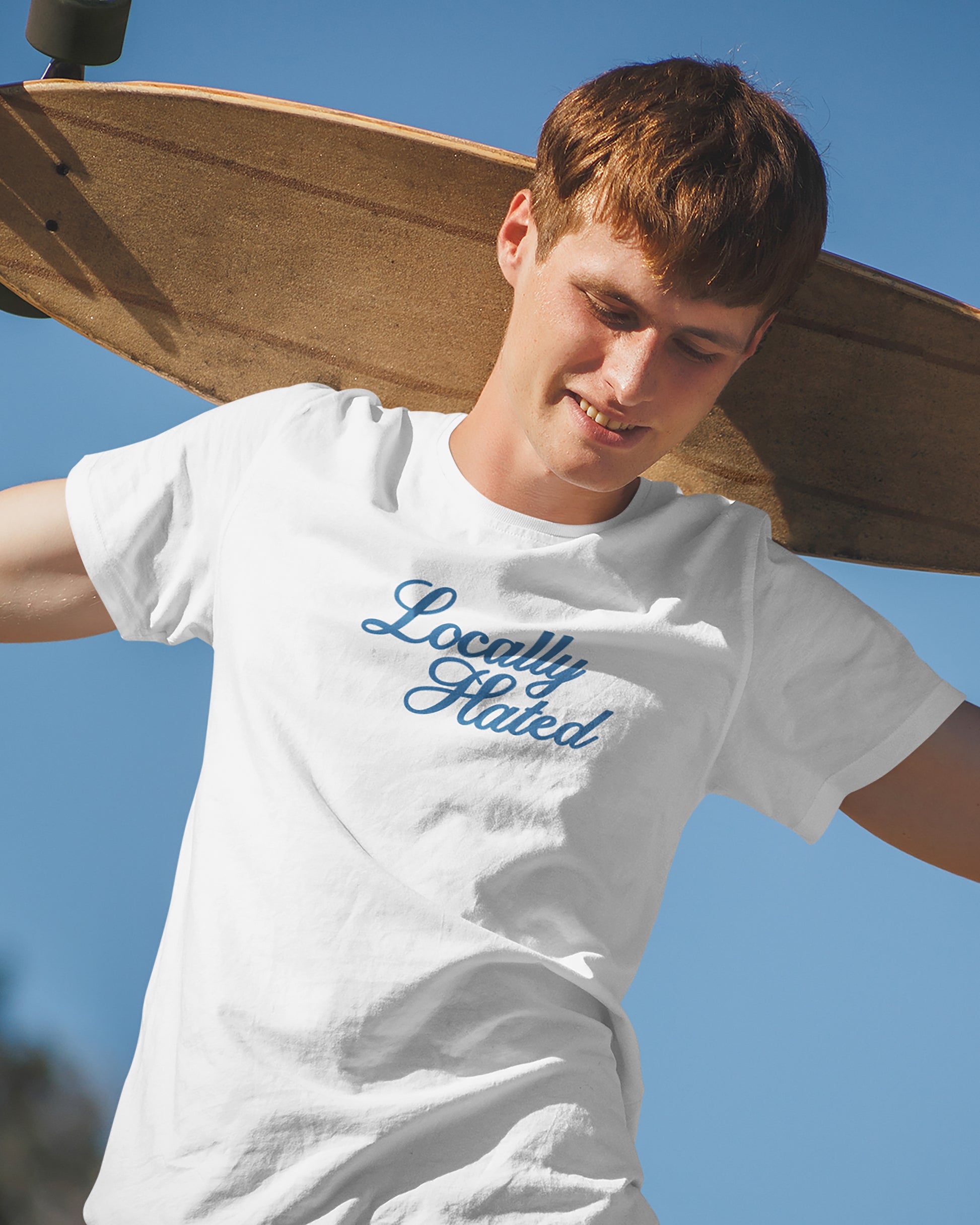 Person wearing a white t-shirt with 'Locally Hated' text, holding a skateboard against a clear blue sky.