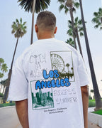 Person wearing a white t-shirt with 'Los Angeles' graphic in front of palm trees