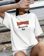 Person wearing a white t-shirt with 'Mozzarella Slut' text and red graphic, sitting on a bench.