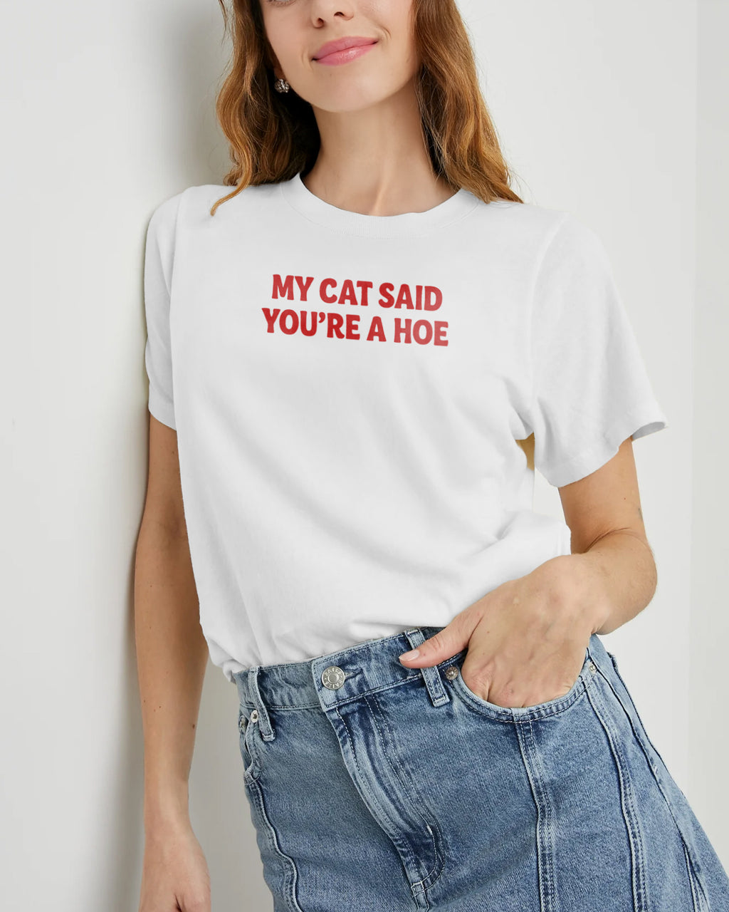 Person wearing a white t-shirt with "My cat said you're a hoe" and blue jeans against a plain background