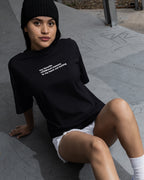 Person wearing a black t-shirt with text, sitting on a concrete surface.