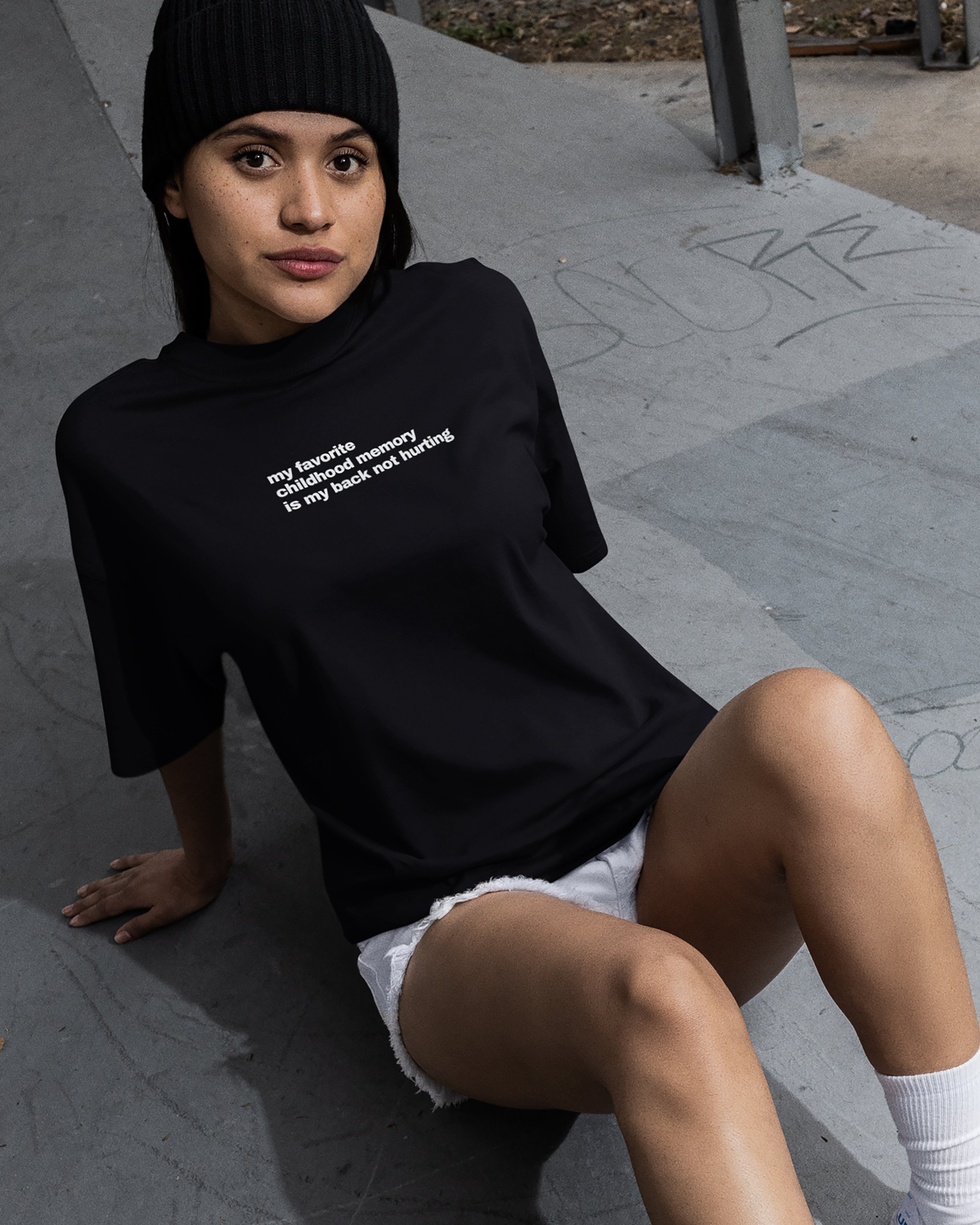 Person wearing a black t-shirt with text, sitting on a concrete surface.