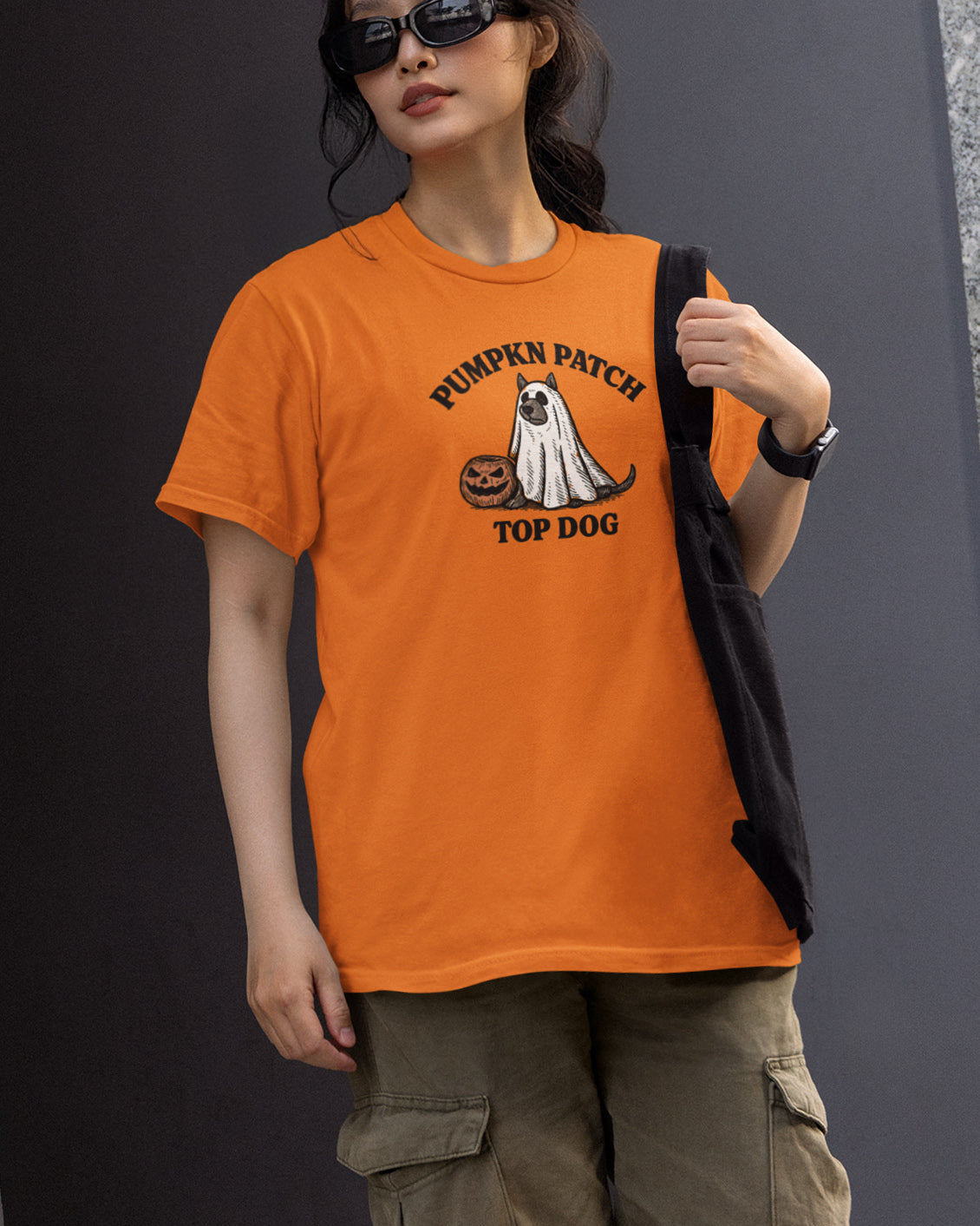 Person wearing an orange t-shirt with a ghost and pumpkin design, standing against a dark background.