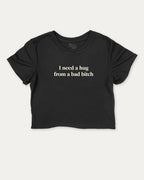 I Need A Hug From A Bad Bitch graphic crop tee with funny and trendy slogan print, perfect for women’s casual looks or layering. Black crop t-shirt.