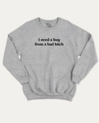 I Need A Hug From A Bad Bitch graphic sweatshirt with bold and funny print, warm and cozy graphic for everyday wear. Perfect for adults and gift-giving. Heather Grey pullover.