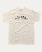 I Need A Hug From A Bad Bitch graphic tee with bold and funny print, funny and trendy graphic. Perfect for adults and gift-giving. Cream shirt.