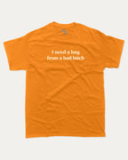 I Need A Hug From A Bad Bitch graphic tee with bold and funny print, funny and trendy graphic. Perfect for adults and gift-giving. Orange shirt.