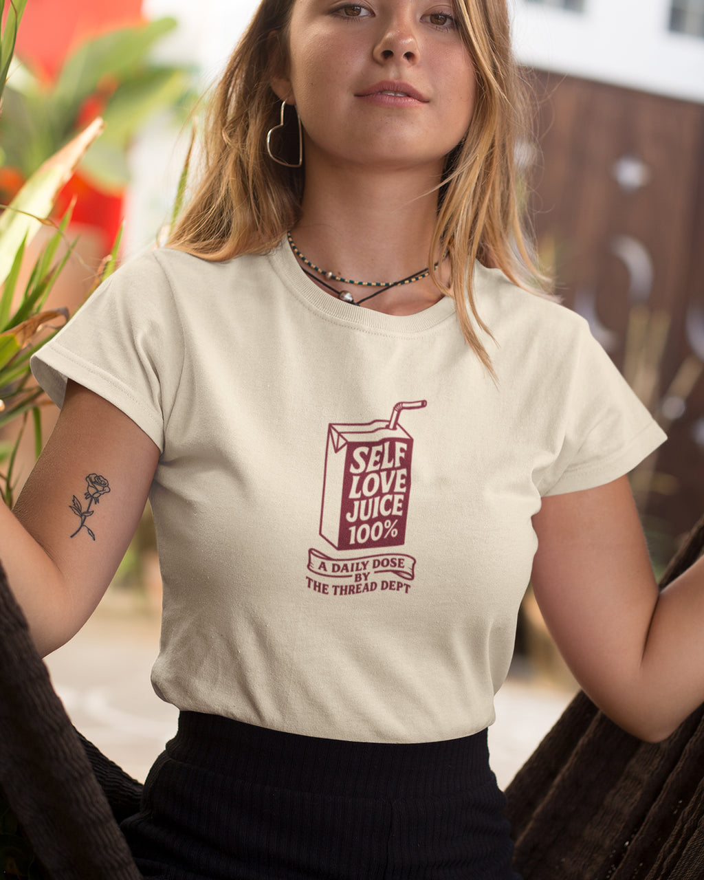 Person wearing a white t-shirt with a graphic design of 'Self Love Juice' on a blurred outdoor background