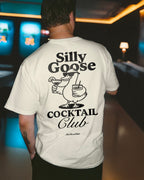 Person wearing a white t-shirt with 'Silly Goose Cocktail Club' design in a bar setting