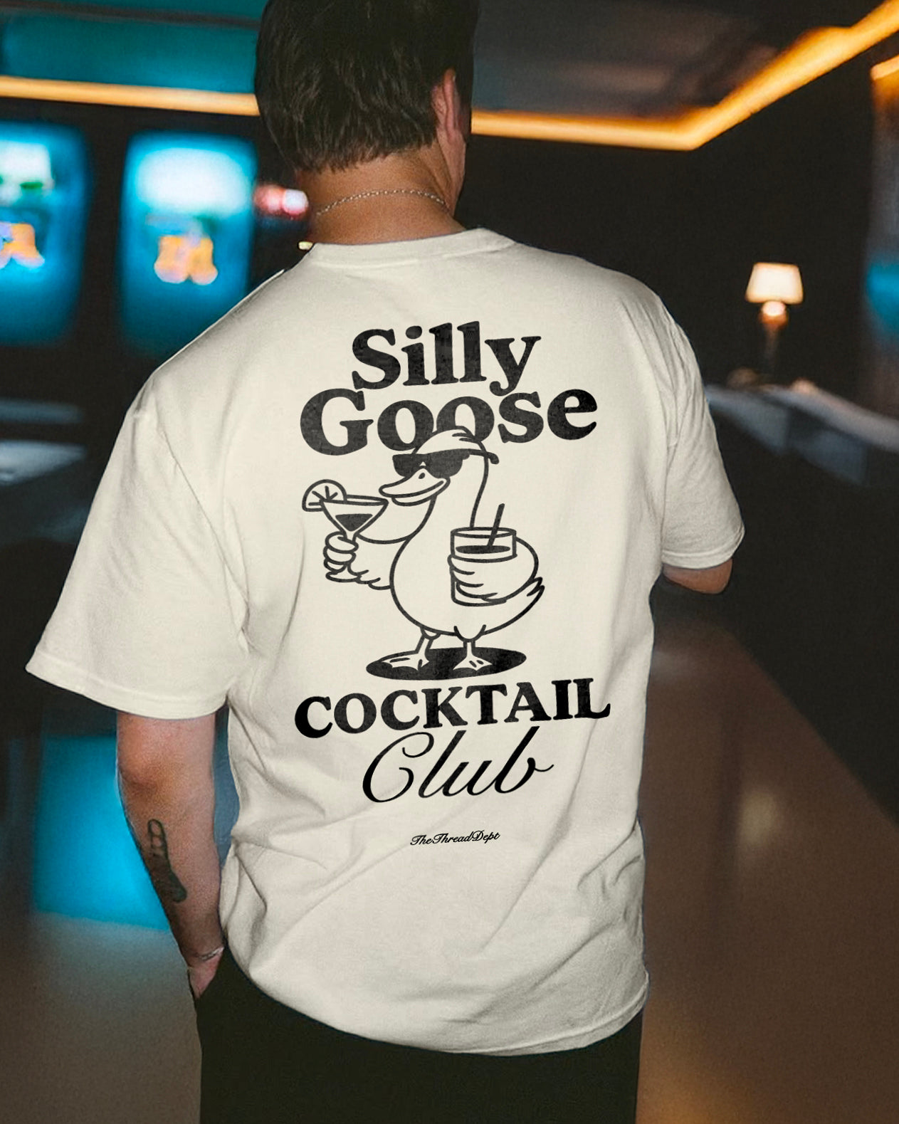 Person wearing a white t-shirt with 'Silly Goose Cocktail Club' design in a bar setting