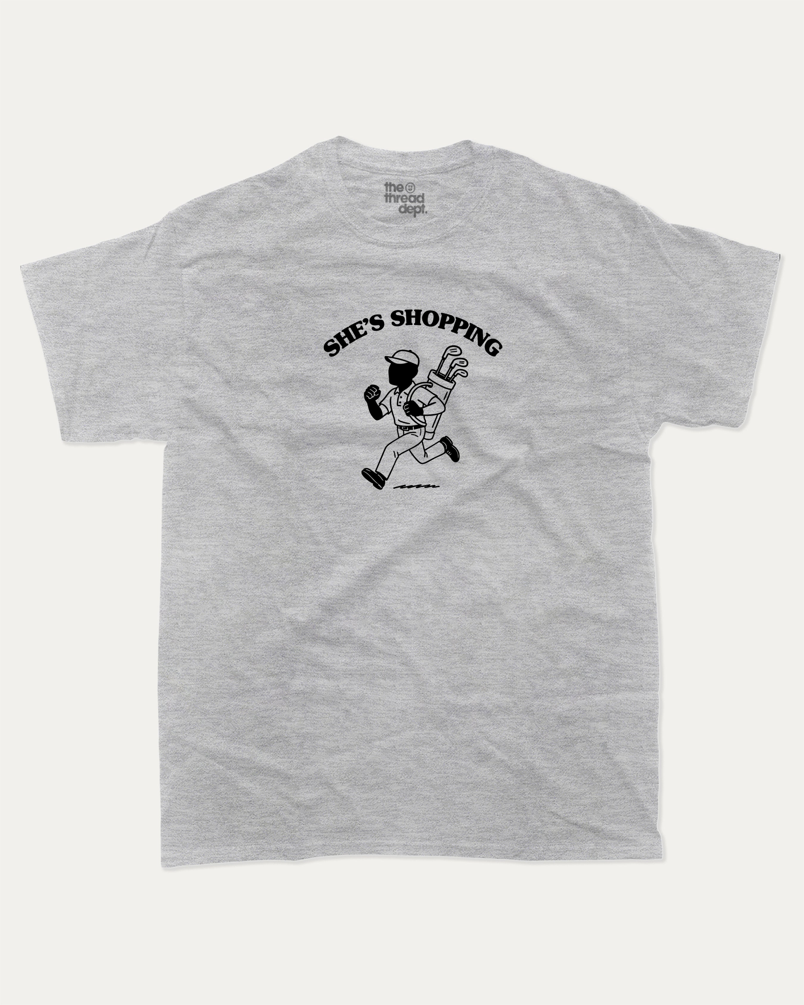 She's Shopping graphic tee with bold and humorous print, Golf Graphic T shirt, Perfect Gift for Golf Lover,  funny and trendy graphic. Perfect for adults and gift-giving. Heather Grey shirt.