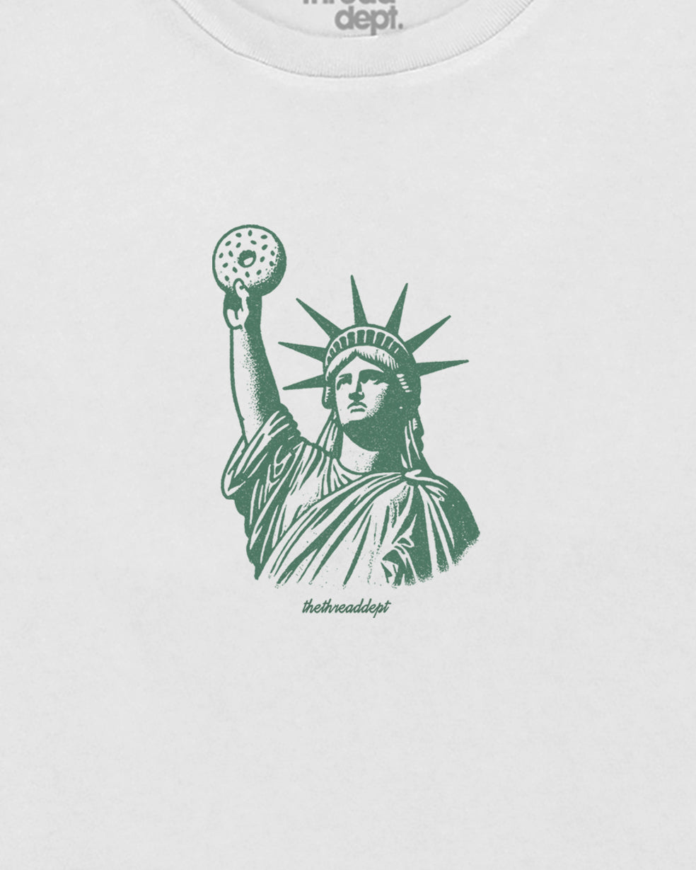 White t-shirt with green graphic of the Statue of Liberty holding a bagle.