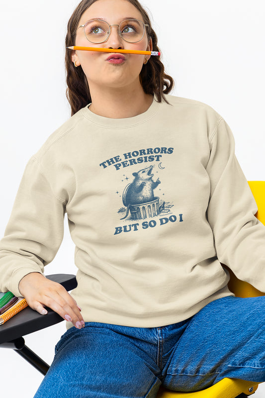 Person wearing a beige sweatshirt with a graphic and text, sitting on a chair.