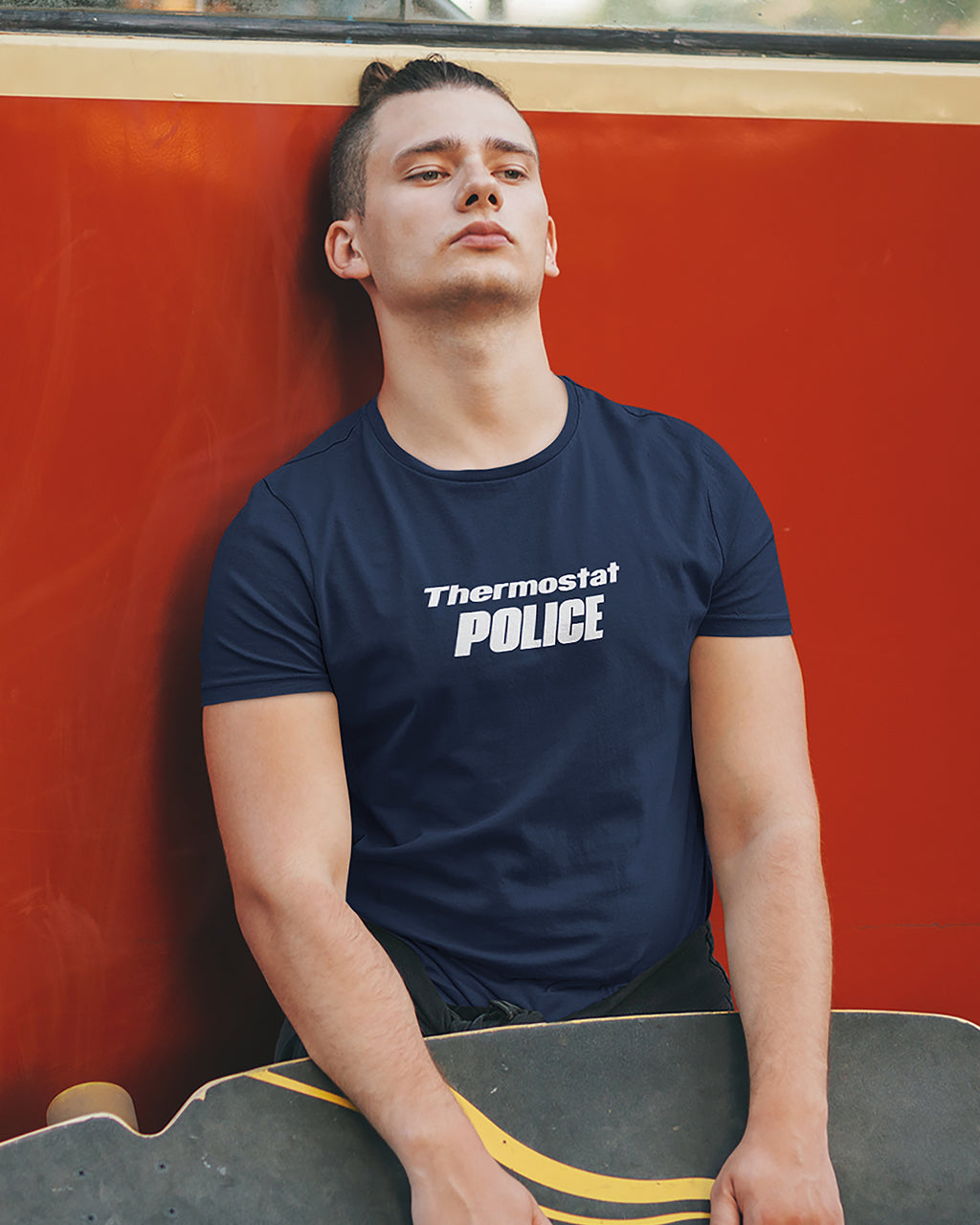 Person wearing a navy blue t-shirt with 'Thermostat POLICE' text, sitting against a red wall.